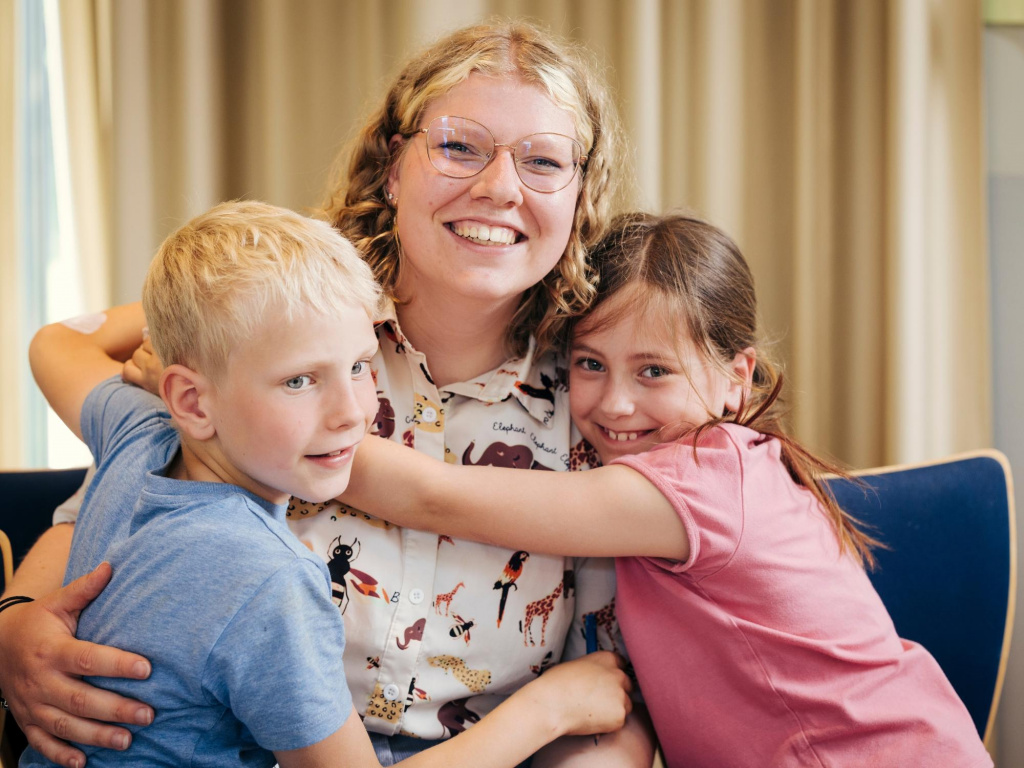 Die Freiwillige und zwei Kinder lächeln in die Kamera.